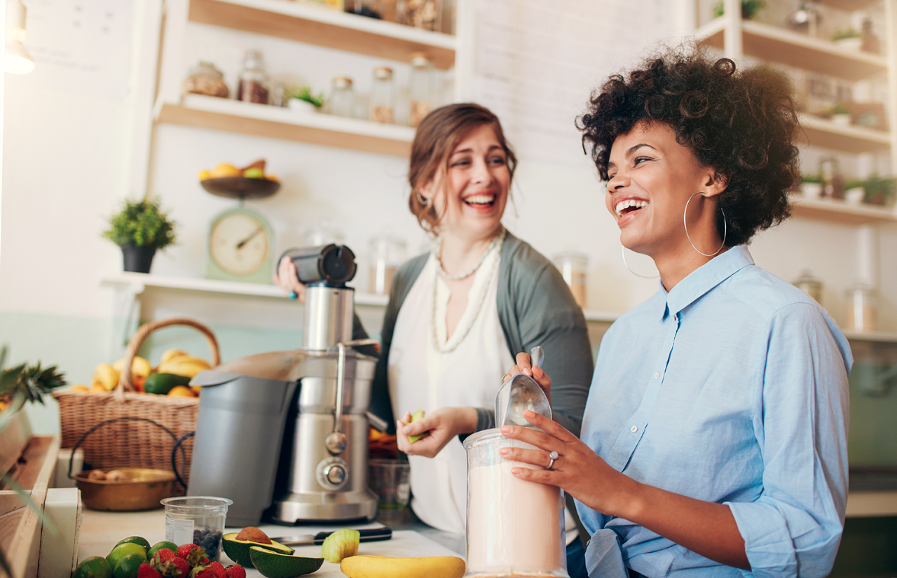 Two young women talking and smiling while working at bar counter. They are preparing fruit juice.; Shutterstock ID 441297520; Purchase Order: E&I library